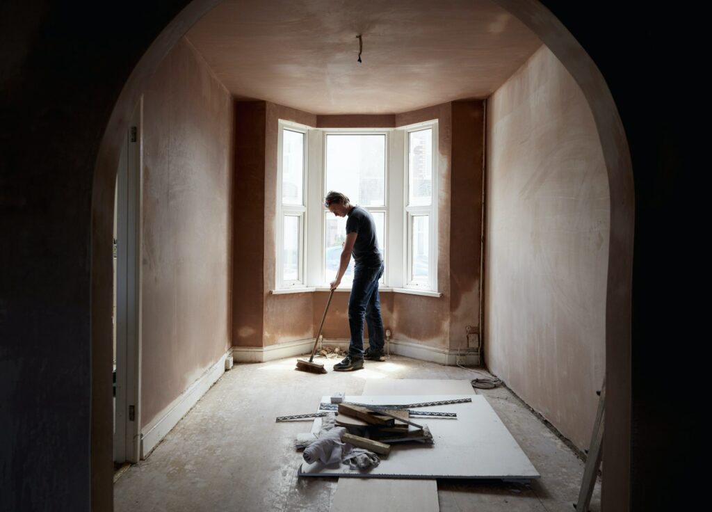 A builder sweeping and tidying up in a renovated replastered house with an archway.